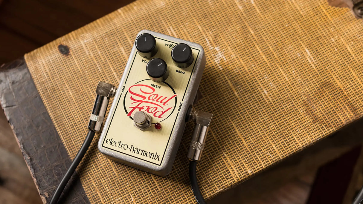 Electro-Harmonix Soul Food transparent overdrive guitar pedal on wooden surface with black cables connected to input/output jacks, showcasing Volume/Treble/Drive knobs, illuminated red LED footswitch engaged, and red Soul Food logo for analog distortion effects