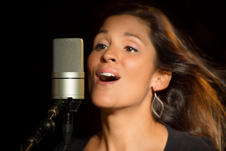 Female singer performing into MXL 990 condenser microphone on stand against black background