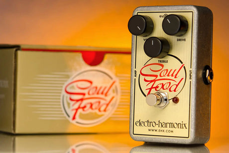 Electro-Harmonix Soul Food transparent overdrive guitar pedal angled view on orange gradient with matching box packaging, showcasing Volume/Treble/Drive knobs, illuminated footswitch, and red Soul Food logo for analog fuzz/distortion effects