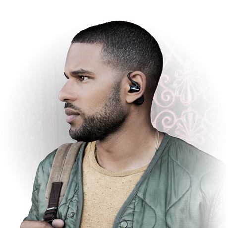 Side profile of a man with short hair, beard, wearing a green jacket and backpack, using Shure RMCE-TW2 True Wireless Secure Fit Adapter Gen 2 black over-ear hooks with earphones, against a dark background