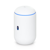A compact, cylindrical white Ubiquiti UniFi Dream Router (UDR) WiFi 6 gateway standing upright on a neutral background, featuring a glossy polycarbonate finish, subtle ventilation on the sides, a blue status LED ring around the dome-shaped top antenna area, and rear Gigabit Ethernet ports including PoE LAN connections for network devices